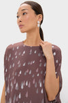 Woman modeling the Polka Rain Eleonore Dress, showcasing a classic, effortless look with its fun teardrop motif, high-end statement earring, and elegant mauve-brown top detail.