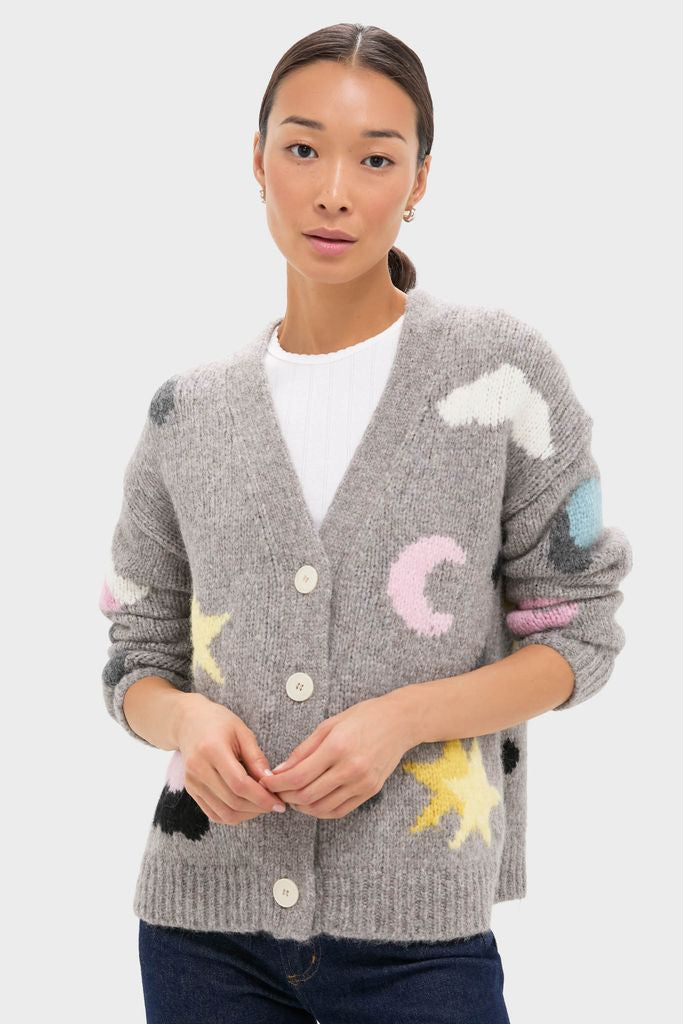Woman models classic Grey Weather Cycles Intarsia Stormy Cardigan with whimsical pastel motifs, showcasing its chunky knit texture and effortless, high-end style.