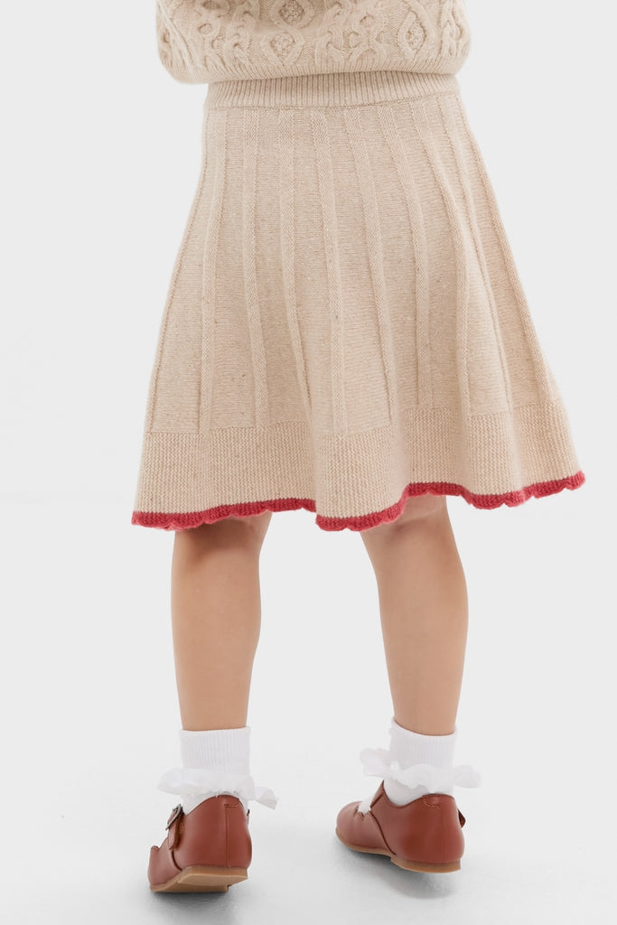 Child in cream Sienna Skirt with classic pleats, red scalloped trim, ruffled socks, and Mary Jane shoes. Effortless, high-end vintage charm for fun, cool style.