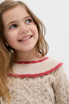 Young girl in a cream Sienna Sweater with ruffled neckline, showcasing classic cable-knit design and effortless style, perfect for fun, high-end cold-weather fashion.