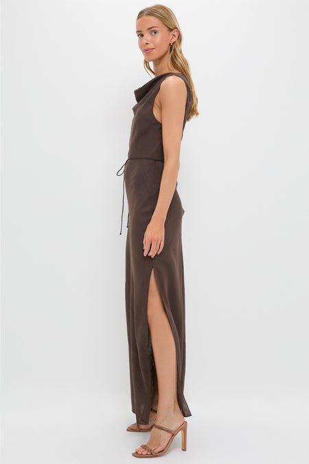 Model in profile wearing the classic Chocolate Serine Maxi Dress, featuring an effortless cowl neckline, drawstring waist, and high slit, paired with strappy high-end sandals.