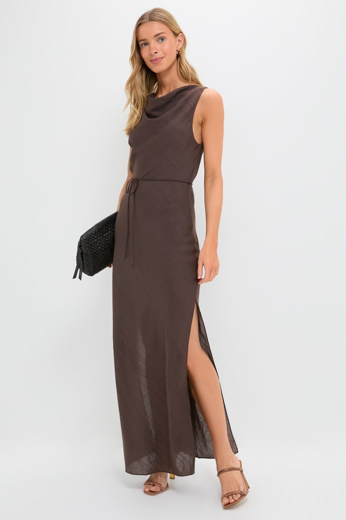 Model wearing the Chocolate Serine Maxi Dress featuring a classic cowl neckline and high side slit. Paired with tan block-heeled sandals and a black clutch, exuding effortless, high-end style.