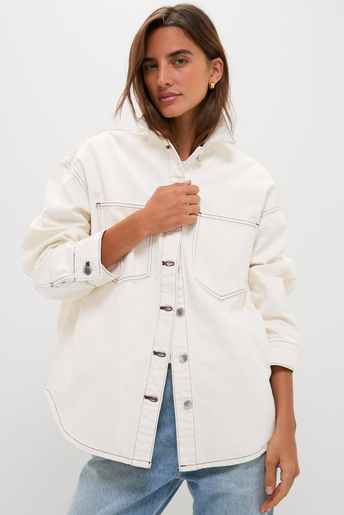 Woman modeling the Natural Bryden Denim Jacket, an oversized, off-white shirt with contrast stitching and large chest pockets, embodying a classic, effortless, high-end style.