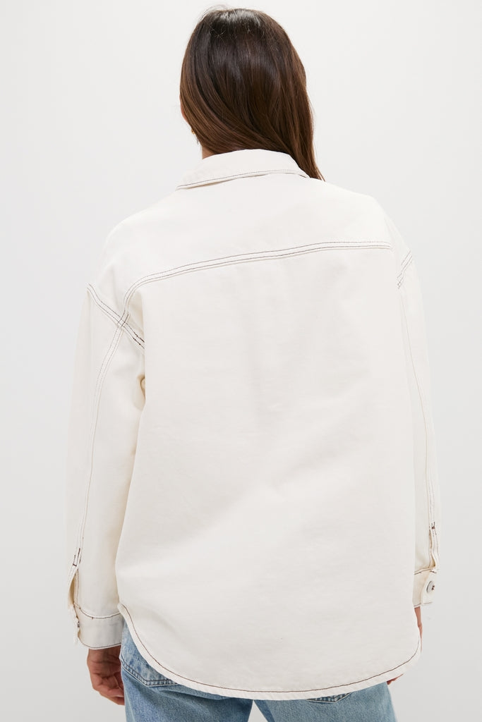 Woman wearing the Natural Bryden Denim Jacket, showcasing its classic, effortless design with contrast stitching, paired with light blue jeans, embodying fun and high-end style.