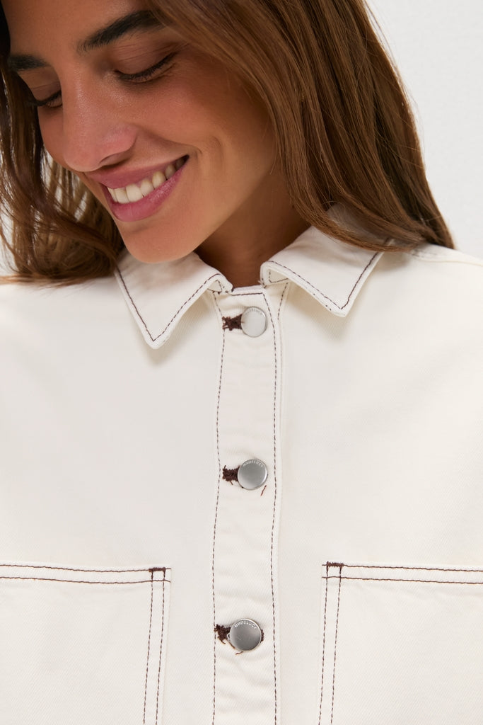 Woman smiling in a classic, Natural Bryden Denim Jacket with a pointed collar and silver snap buttons, exuding effortless, high-end style with a fun, contrasting topstitching detail.