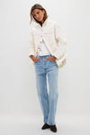 Woman wearing the classic, high-end Natural Bryden Denim Jacket over a white top, paired with light-wash jeans and ankle boots, exuding an effortless and fun style.