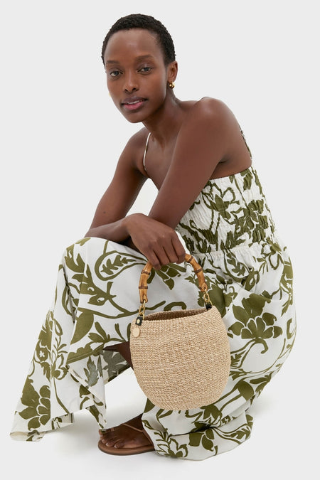 Model wearing the classic Dahlia Maxi Dress with smocked bodice and a-line skirt, accessorized with tan slide sandals and a woven straw handbag for an effortless, high-end summer look.