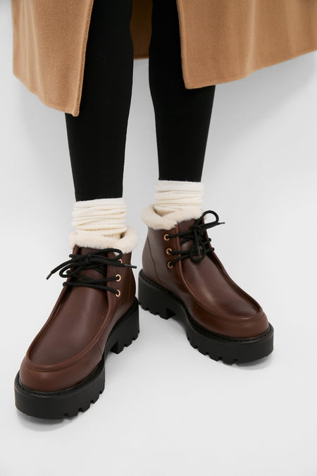 Classic Dark Brown Percy Boots with chunky lug soles, cream shearling cuffs, and black laces, styled with slouchy socks and leggings for an effortless, high-end look.