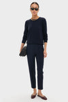 Woman in classic Navy Audrey Pants, styled effortlessly with a dark sweater and burgundy flats, accessorized with gold jewelry and a quilted clutch for a high-end look.