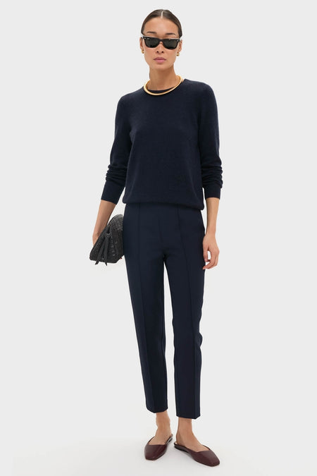 Woman in classic Navy Audrey Pants, styled effortlessly with a dark sweater and burgundy flats, accessorized with gold jewelry and a quilted clutch for a high-end look.