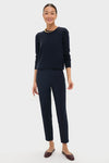 Woman in Navy Audrey Pants, classic and effortless, styled with a navy sweater and burgundy mules. Features pinched seams and zipper closure for a high-end, fun look.