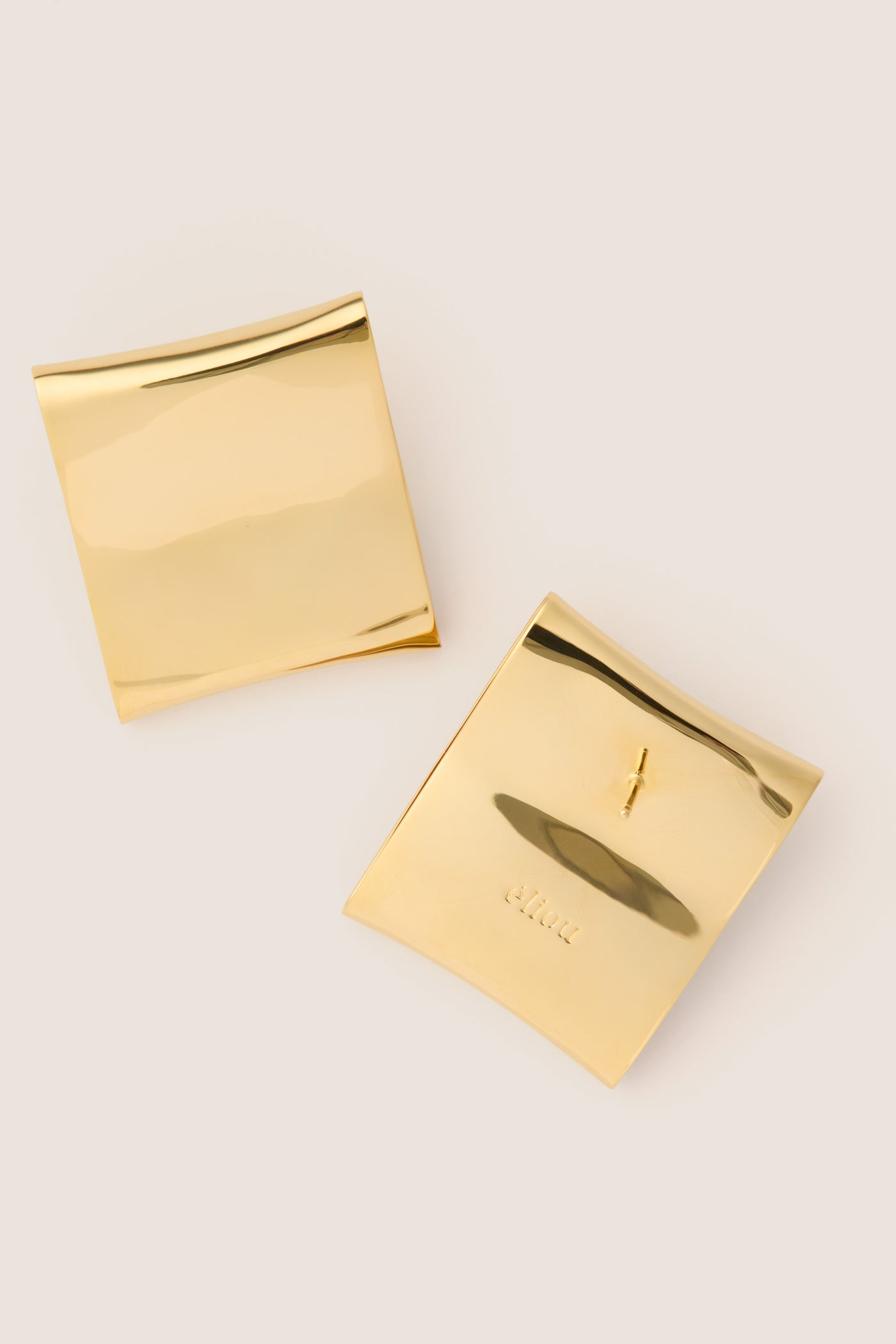 Gold Plated Colbi Earrings pinned on polished gold pouches, showcasing classic, geometric design. Effortlessly elevate your style with these high-end, fun, and lightweight studs.