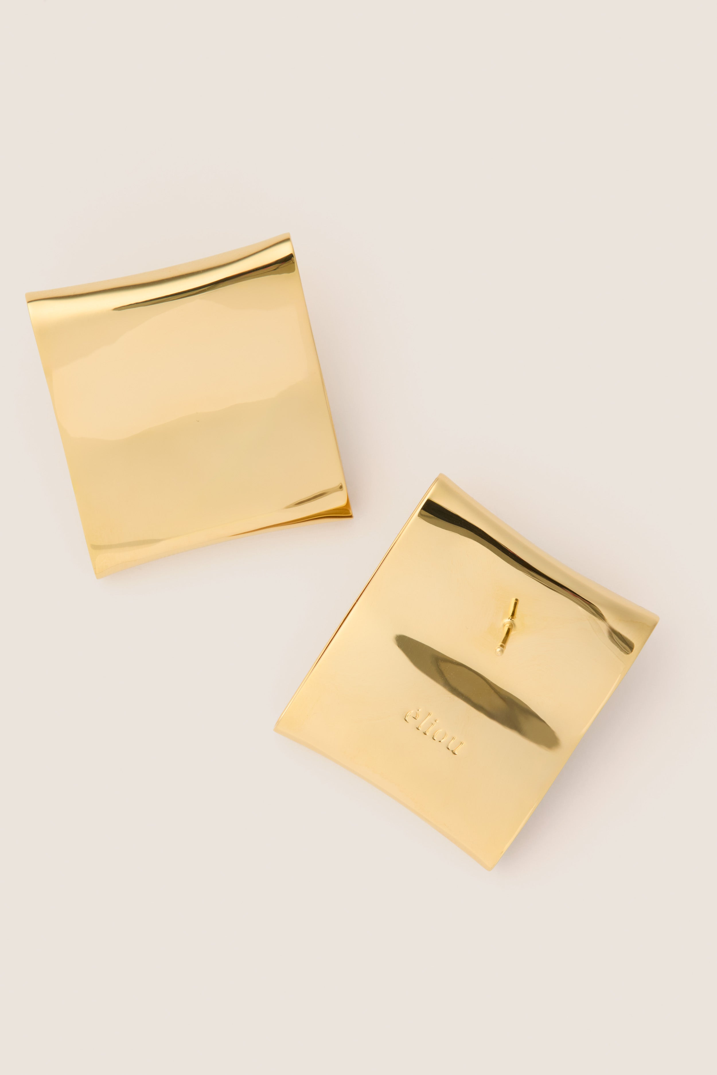 Gold Plated Colbi Earrings pinned on polished gold pouches, showcasing classic, geometric design. Effortlessly elevate your style with these high-end, fun, and lightweight studs.