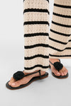 Classic Black Flor Rose Wrap Sandals with a toe-post design and braided rosette detail, paired with wide-leg knit trousers, embody an effortless, high-end style.