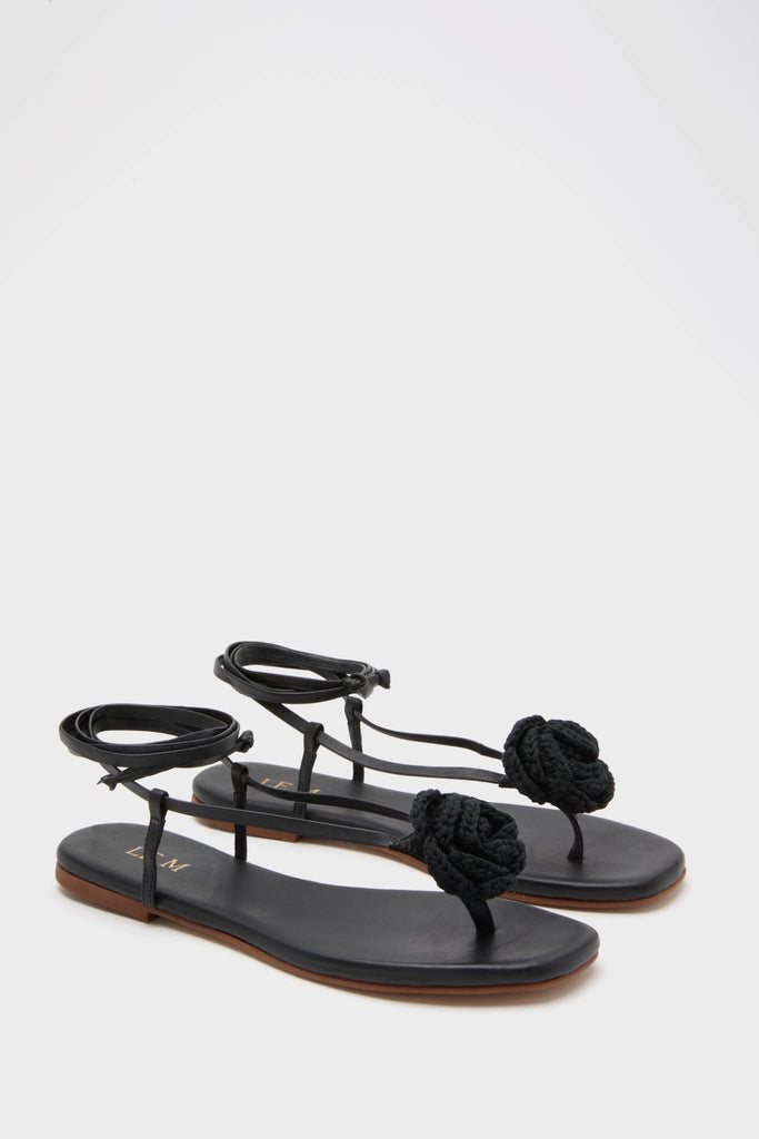 Black Flor Rose Wrap Sandals: classic thong-style with braided rosette detail, effortless flat footbed, and fun ankle wrap straps, embodying a high-end, stylish vibe.