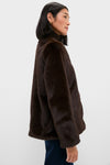 Young woman in profile wears a classic, dark brown Cassidy Faux Fur Jacket, embodying effortless style. The plush, high-end jacket features front closures, perfect for fun winter outings.