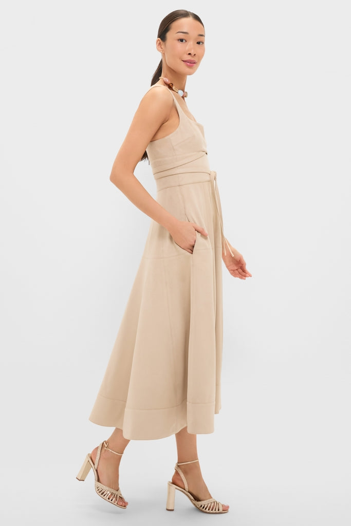 Woman models the classic Dune Suede Kendra Maxi Dress, featuring an effortless sleeveless design, fitted bodice, flared skirt, self-tie belt, and discreet side pockets.