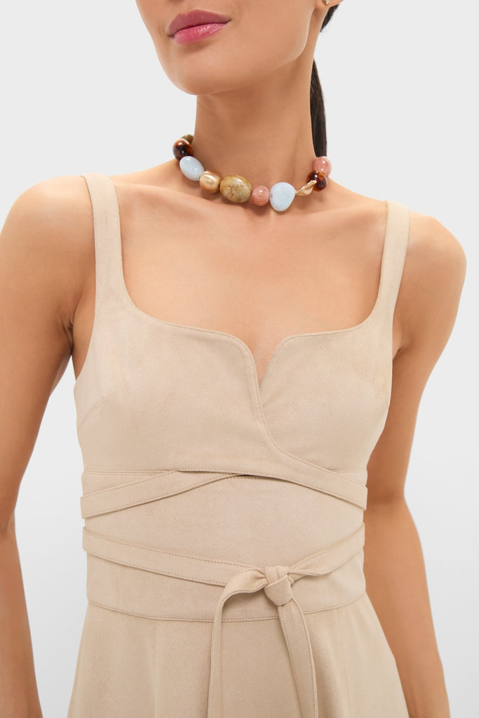 Woman wearing the Dune Suede Kendra Maxi Dress, a classic sleeveless light-beige dress with a square neckline and effortless self-tie waist, paired with a fun, high-end beaded necklace.