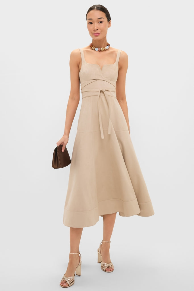 Woman in Dune Suede Kendra Maxi Dress with a square neck and self-tie waist, paired with a beaded necklace, clutch, and block-heeled sandals for an effortless, high-end look.
