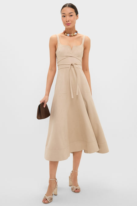 Woman in Dune Suede Kendra Maxi Dress with a square neck and self-tie waist, paired with a beaded necklace, clutch, and block-heeled sandals for an effortless, high-end look.