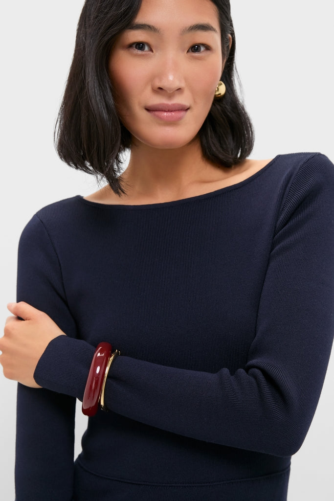 Woman in a navy boat-neck sweater, showcasing classic, effortless style. Burgundy and gold bracelets and earring complement her look, embodying Tuckernuck's high-end, fun fashion ethos.