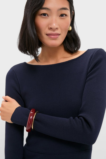 Woman in a navy boat-neck sweater, showcasing classic, effortless style. Burgundy and gold bracelets and earring complement her look, embodying Tuckernuck's high-end, fun fashion ethos.