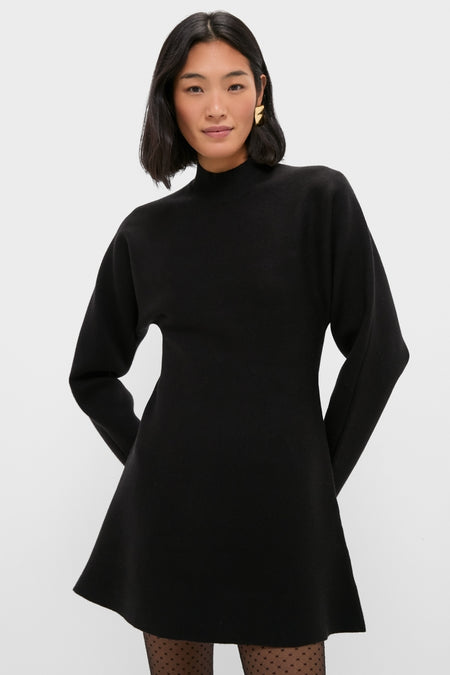 Person wearing a classic Black Anzu Peplum Sweater Mini Dress with an A-line skirt, sheer polka-dot tights, and a sculptural gold earring, exuding effortless, high-end style.