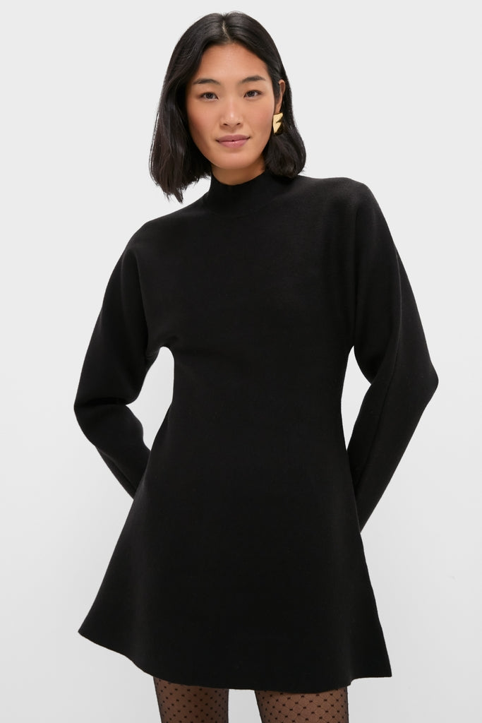 Person wearing a classic Black Anzu Peplum Sweater Mini Dress with an A-line skirt, sheer polka-dot tights, and a sculptural gold earring, exuding effortless, high-end style.