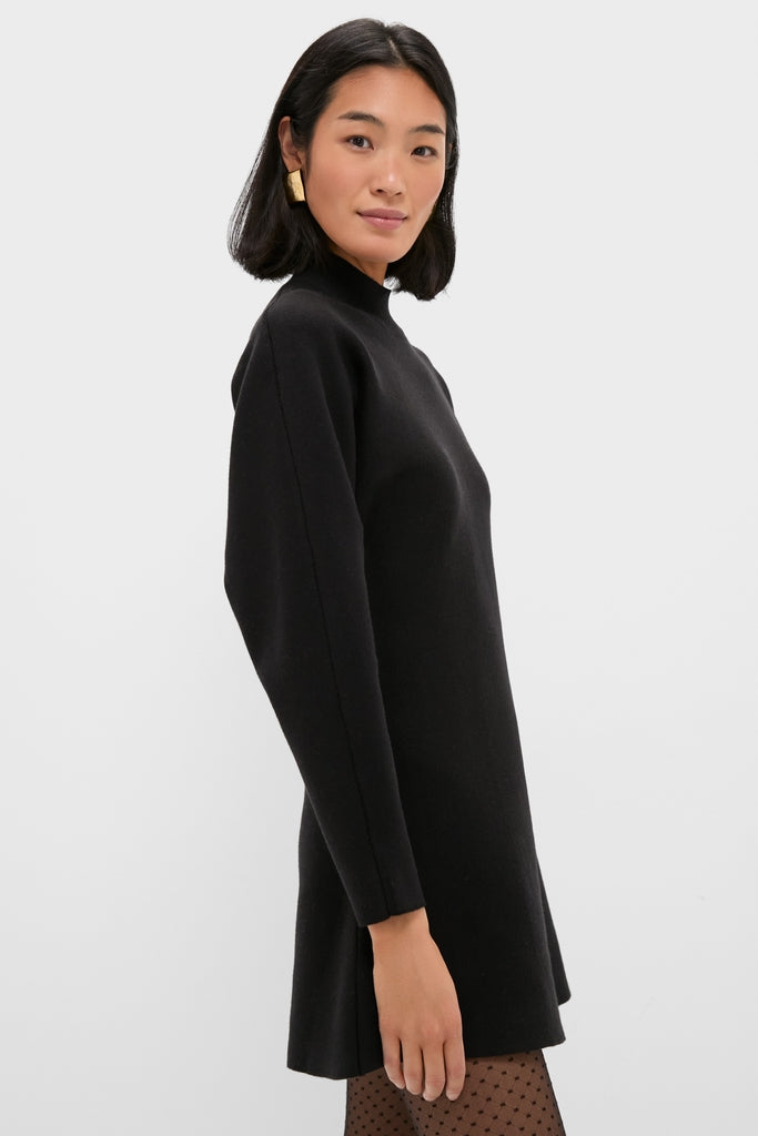 Young woman in Black Anzu Peplum Sweater Mini Dress, paired with sheer dotted tights and a chunky gold-tone earring, showcasing a classic, effortless, and high-end look.