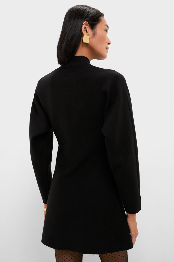 Woman in profile wearing the Black Anzu Peplum Sweater Mini Dress, sheer polka-dot tights, chunky gold earring, and slim gold bangle, embodying classic, effortless style.