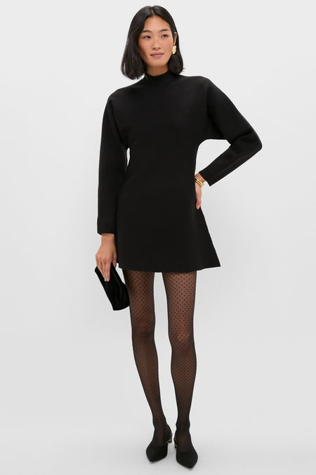 Model wearing the classic Black Anzu Peplum Sweater Mini Dress, paired with sheer polka-dot tights, black heels, and gold accessories, showcasing an effortless, high-end style.