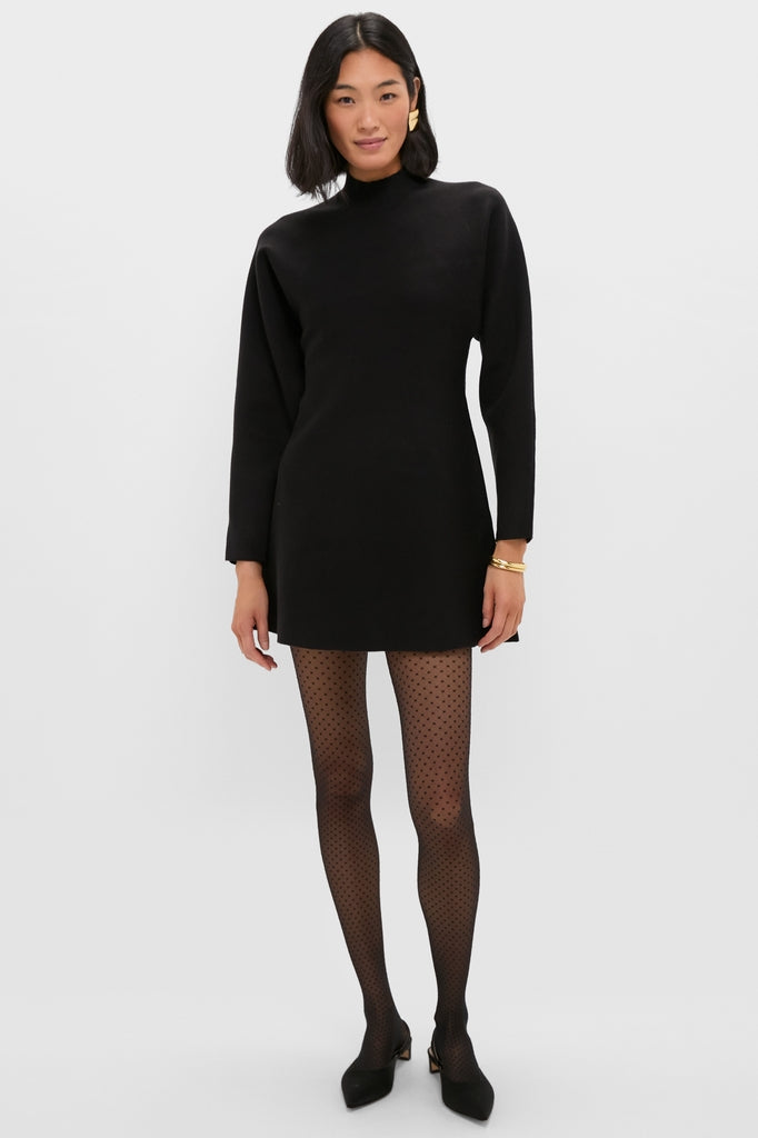 Model wearing the classic Black Anzu Peplum Sweater Mini Dress with sheer polka-dot tights and gold jewelry, embodying effortless, high-end style for an exciting, fun look.