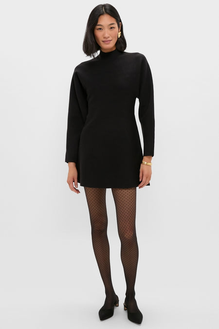 Model wearing the classic Black Anzu Peplum Sweater Mini Dress with sheer polka-dot tights and gold jewelry, embodying effortless, high-end style for an exciting, fun look.