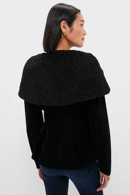 Black Geneva Jacket with a classic sherpa-style collar, effortlessly draped over shoulders. Paired with dark blue jeans, embodying a fun, high-end fashion for modern women.