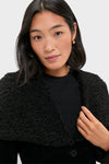 Woman modeling the Black Geneva Jacket, featuring a textured design and wide curly-fleece collar, effortlessly paired with a black top and gold hoop earring.