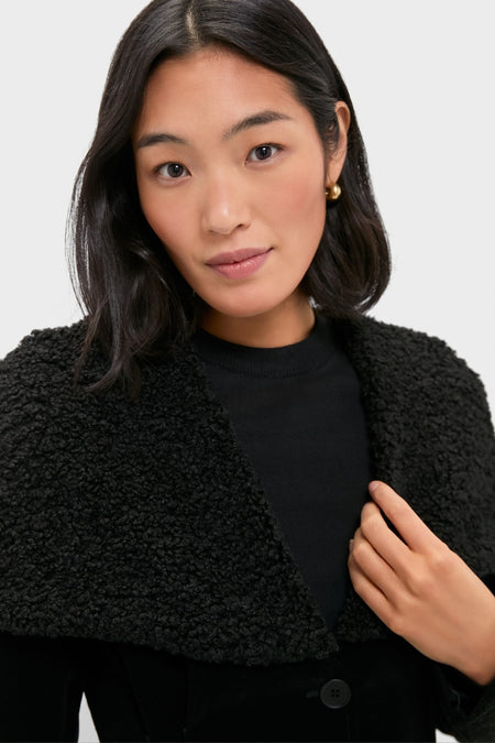 Woman modeling the Black Geneva Jacket, featuring a textured design and wide curly-fleece collar, effortlessly paired with a black top and gold hoop earring.