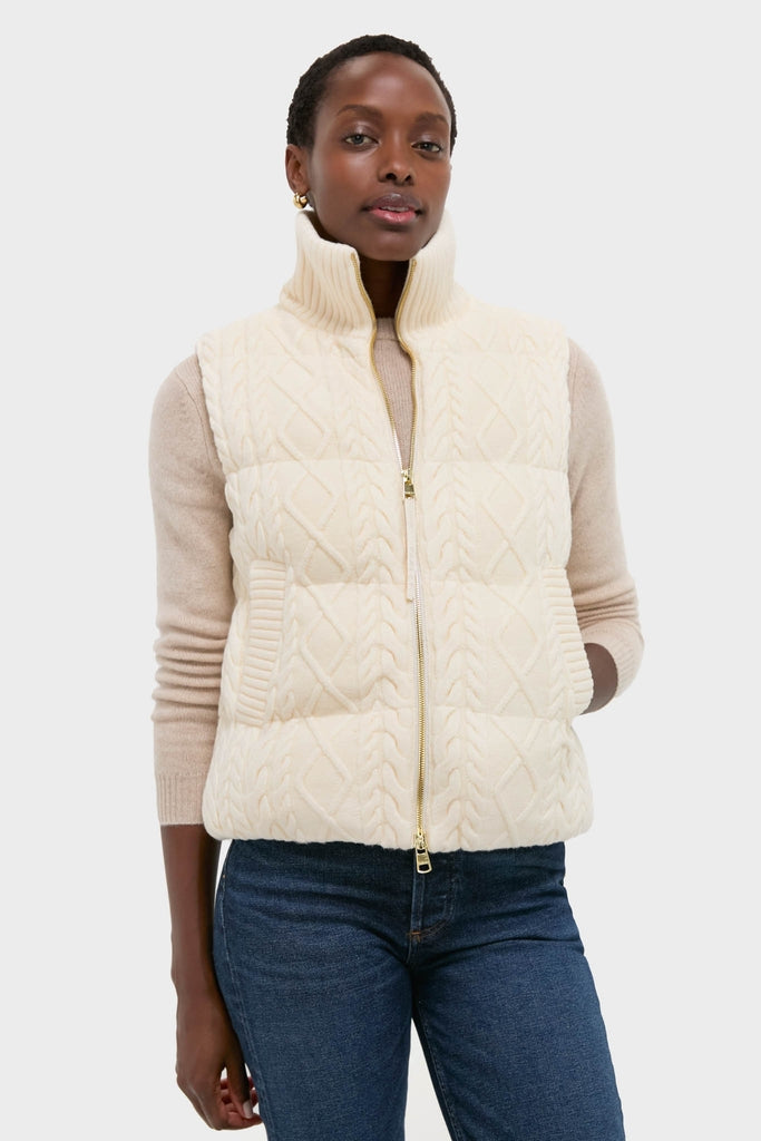 Woman models Egret Irina Cable Knit Gilet, a classic, sleeveless quilted vest featuring a high ribbed collar, gold-tone zipper, and effortless cable-knit design over a long-sleeve top.