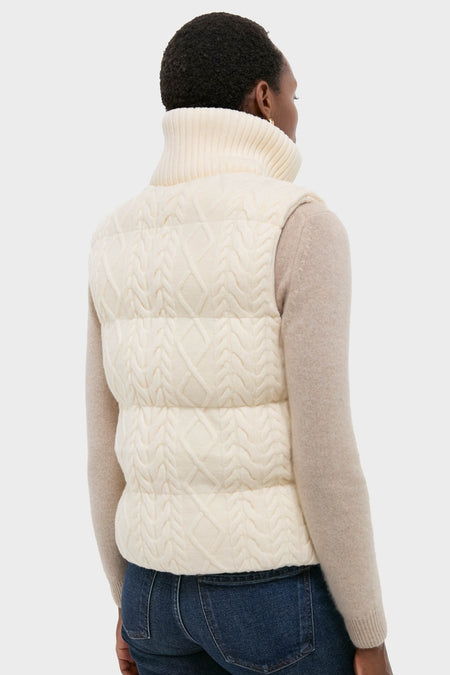 Woman in cream cable-knit Egret Irina Gilet with ribbed collar over beige sweater and blue jeans, showcasing an effortless, high-end, classic outerwear style.