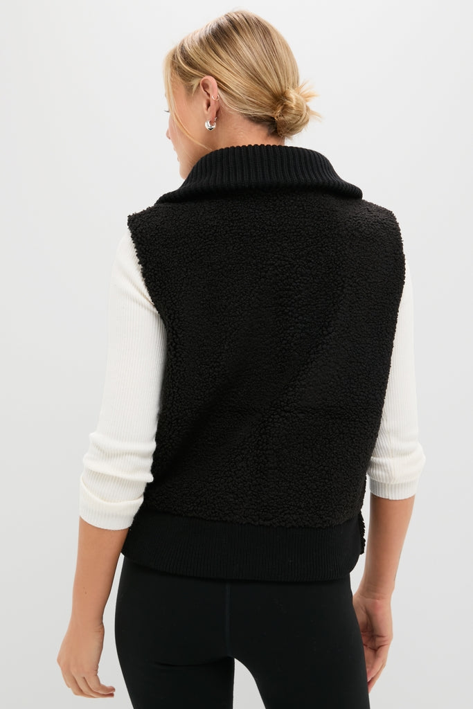 Model wearing the Black Caspian Sherpa Gilet, a classic, high-end zip-up vest with a wide ribbed collar, over an effortless, fun white ribbed top.