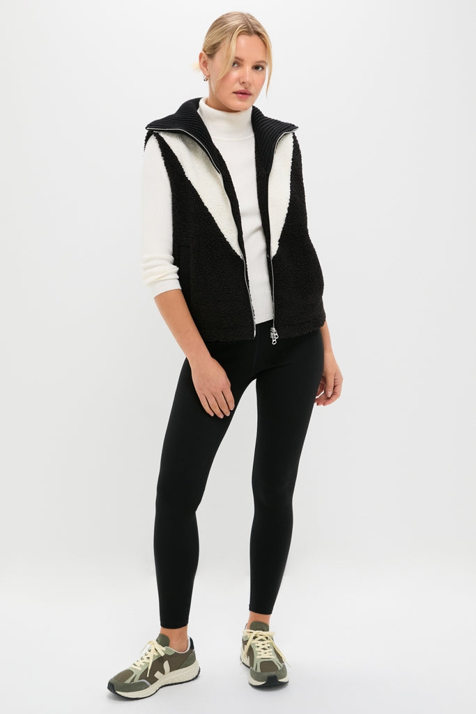 Model wearing the classic Black Caspian Sherpa Gilet over a fitted turtleneck, paired with leggings and lace-up sneakers, showcasing an effortlessly cool and fun high-end style.