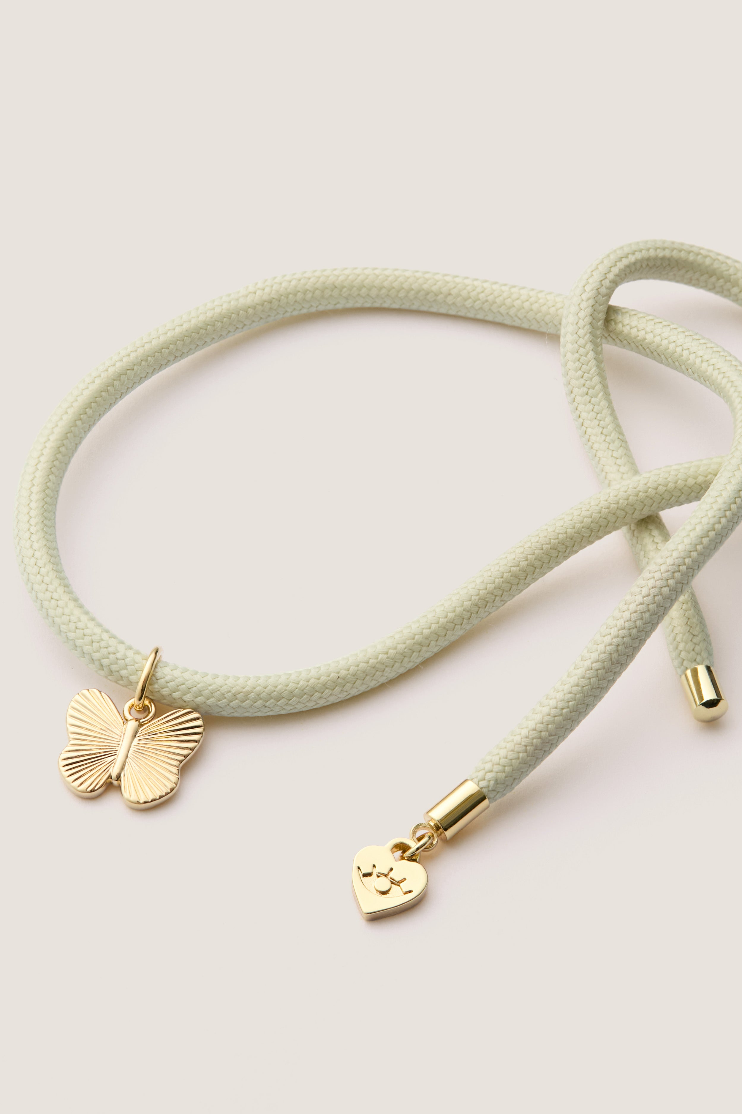 Vineyard Bracelet Cord with Butterfly Charm: A classic, mint-green braided cord with gold-tone caps, featuring a butterfly and eye-stamped heart charm, offering effortless, high-end style.