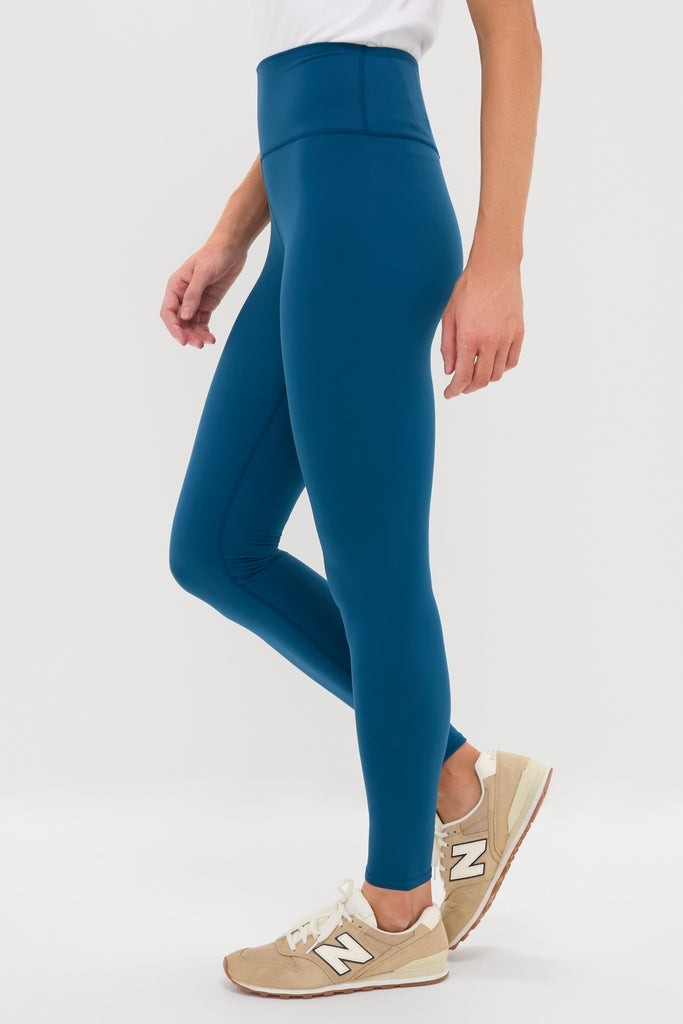 Classic Harbor Blue High Rise Long Compression Spandex MacKenzie Legging, paired with tan New Balance sneakers, showcases an effortless and fun style, perfect for any high-end activity.