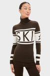 Woman models Chocolate Schild Sweater, a classic, high-end slim-fit turtleneck with SKI detail and star sleeve, effortlessly combining fun style with warmth.