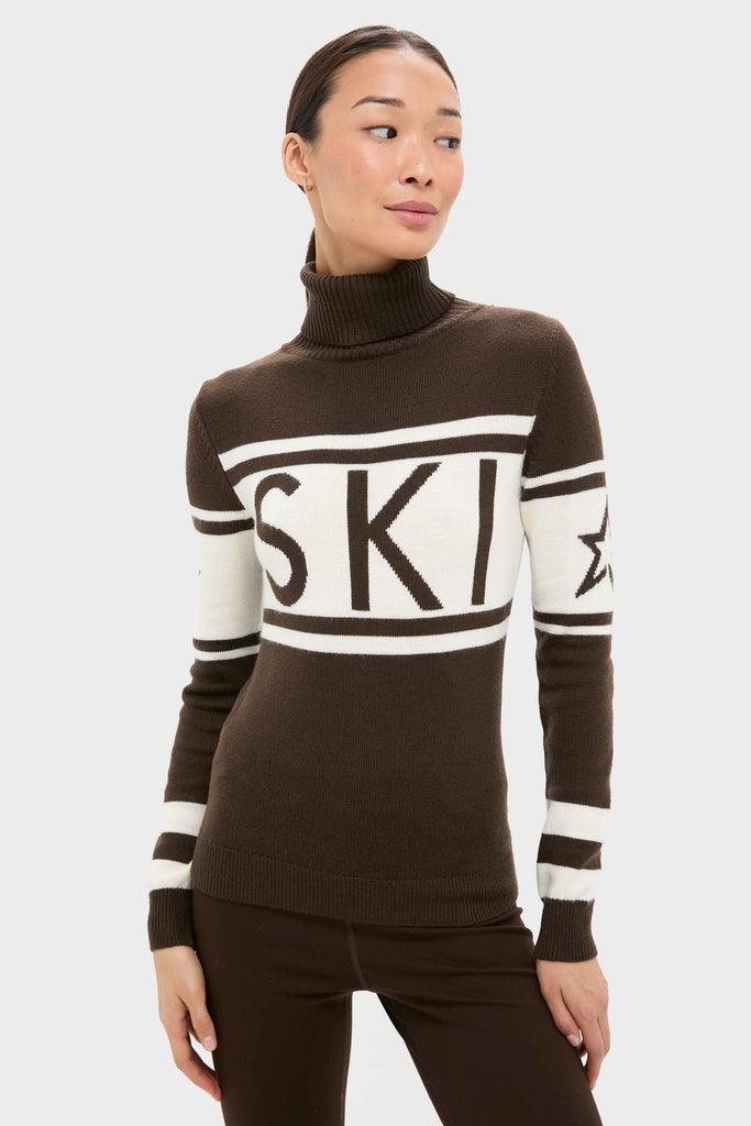 Woman models Chocolate Schild Sweater, a classic, high-end slim-fit turtleneck with SKI detail and star sleeve, effortlessly combining fun style with warmth.