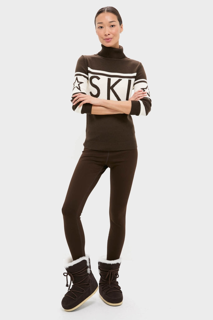 Woman wearing a classic Chocolate Schild Sweater with SKI on chest, paired with brown leggings and fur-lined boots, embodying effortless, high-end style.