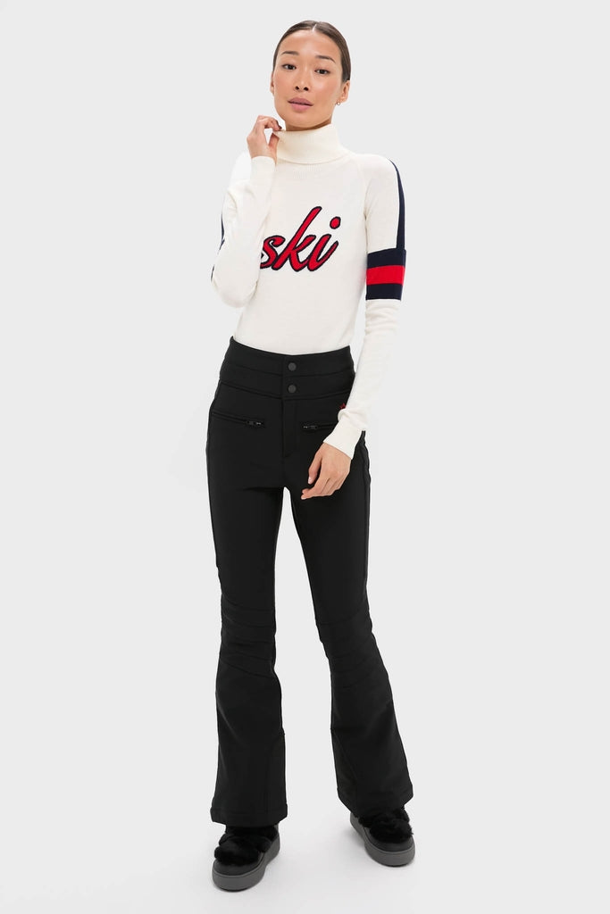 Model wearing the Snow White Neve Wool Sweater, showcasing a classic, high-end alpine look with ski script, paired with slim-fit black ski pants for an effortless, fun style.