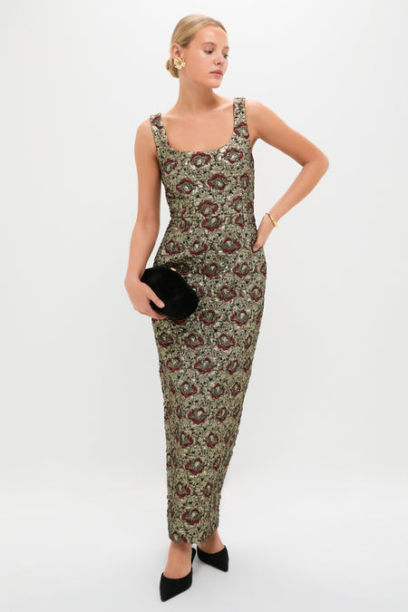 Woman models the Ruby Multi Ravenna Midi Dress with a classic square neckline, featuring an effortless brocade pattern. Paired with a velvet clutch and gold accessories for a high-end look.