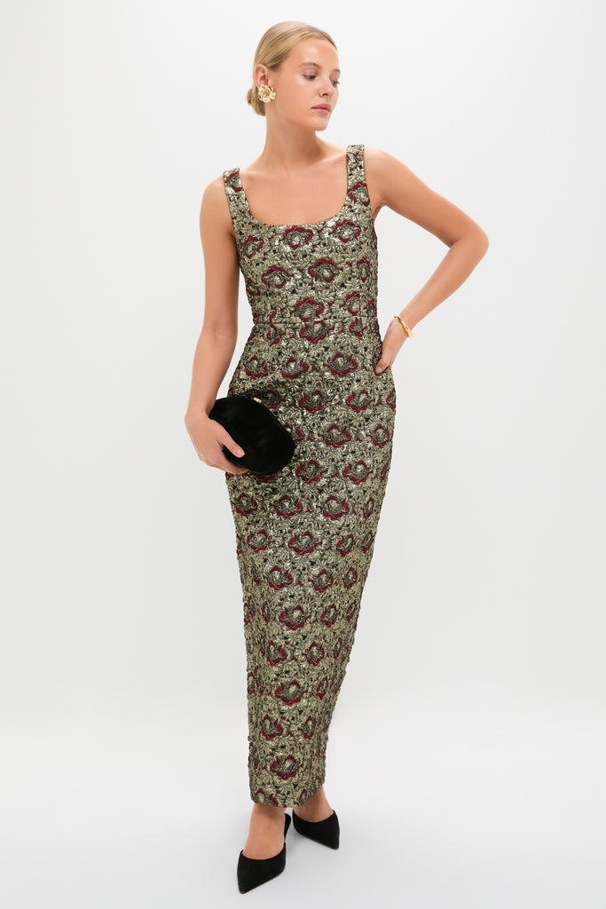 Woman models the Ruby Multi Ravenna Midi Dress with a classic square neckline, featuring an effortless brocade pattern. Paired with a velvet clutch and gold accessories for a high-end look.