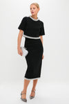 Woman modeling the Black Ozelle Short Sleeve Crewneck Top with beaded trim, paired with a chic pencil skirt, clutch, and pumps; an effortless, classic look for high-end events.