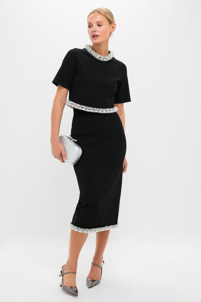 Woman modeling the Black Ozelle Short Sleeve Crewneck Top with beaded trim, paired with a chic pencil skirt, clutch, and pumps; an effortless, classic look for high-end events.